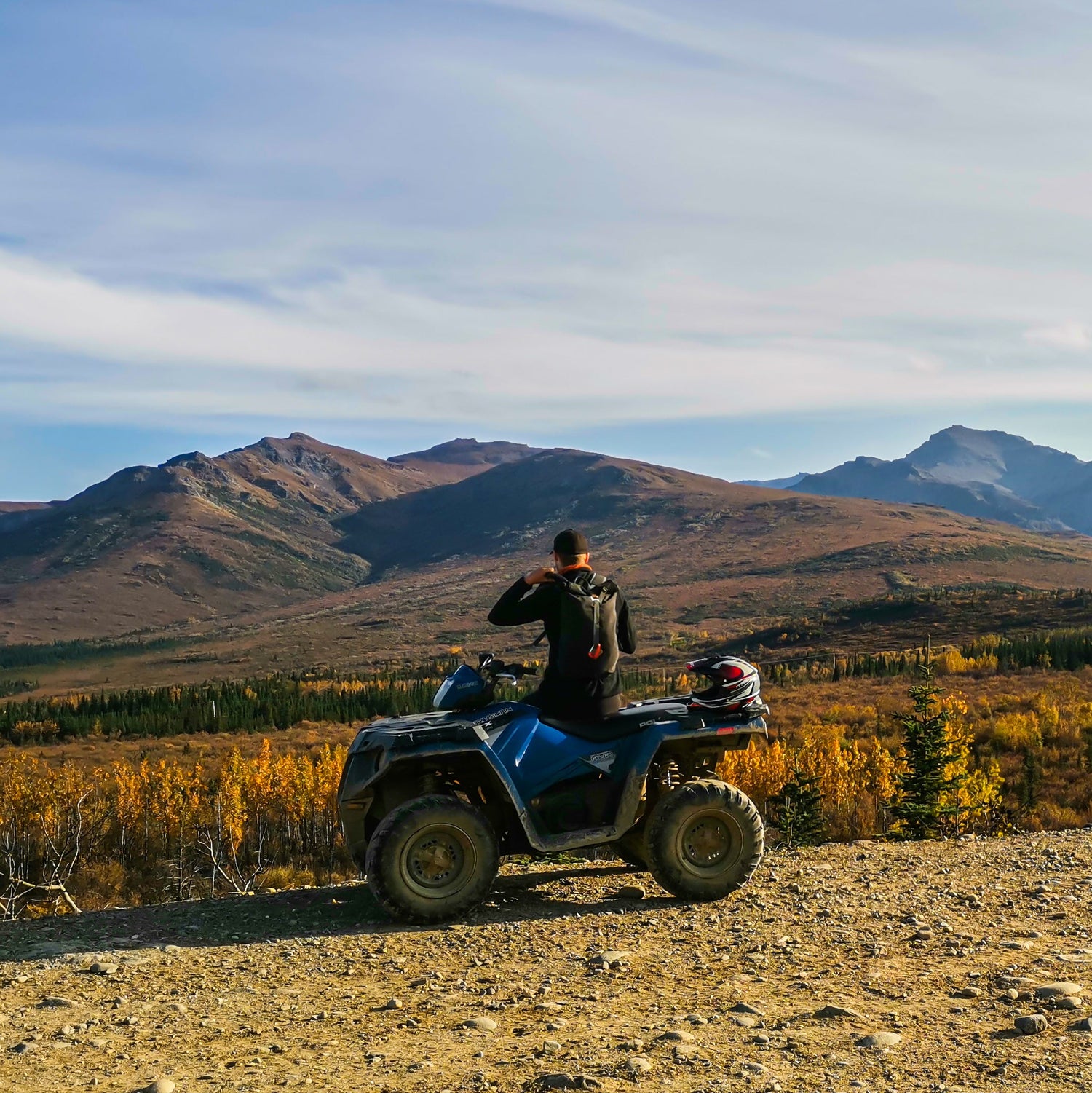 Person on an ATV overlooking a scenic landscape with mountains and trees.